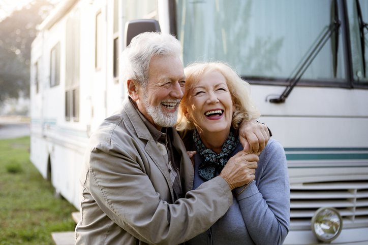 Smiling older couple hugging in front of a parked RV.