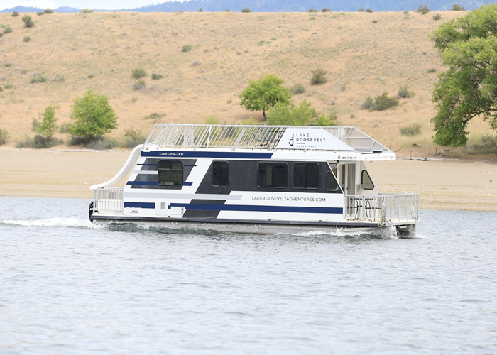 Lake Roosevelt houseboat cruising near a sandy shoreline and hills.