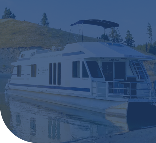 The houseboat docked on a calm lake near a grassy hillside.