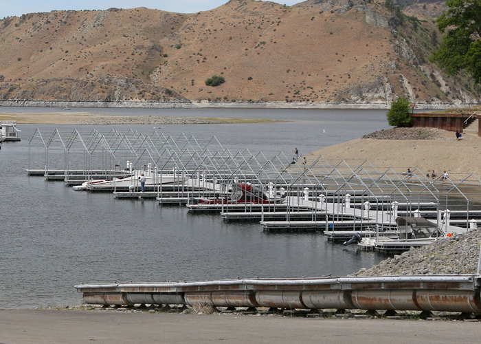 A covered marina boat slips along the shoreline with dry hills across the lake.