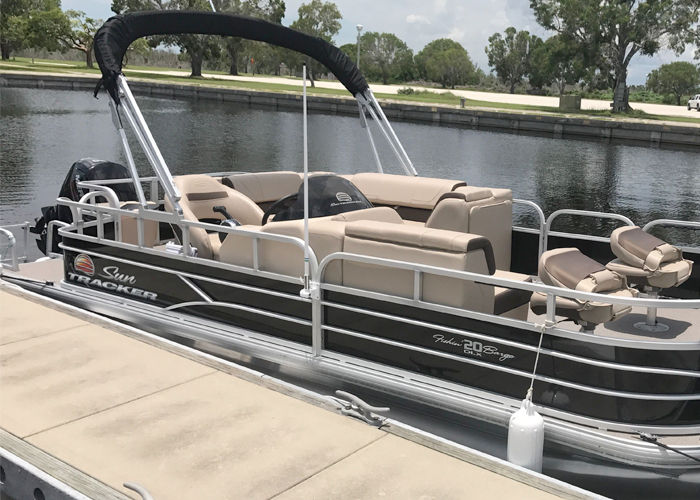 The pontoon boat docked at a marina with cushioned seating and canopy.