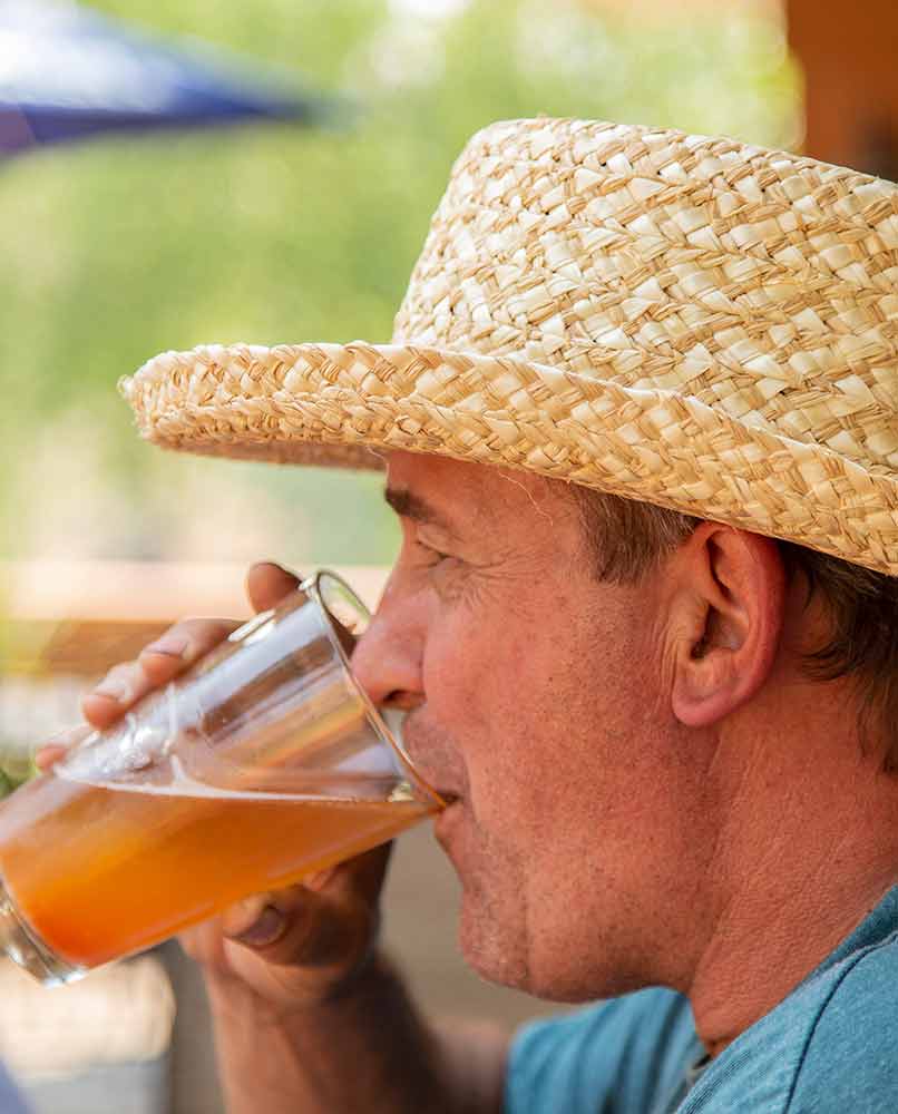 A man wearing a straw hat drinking a glass of beer outdoors.