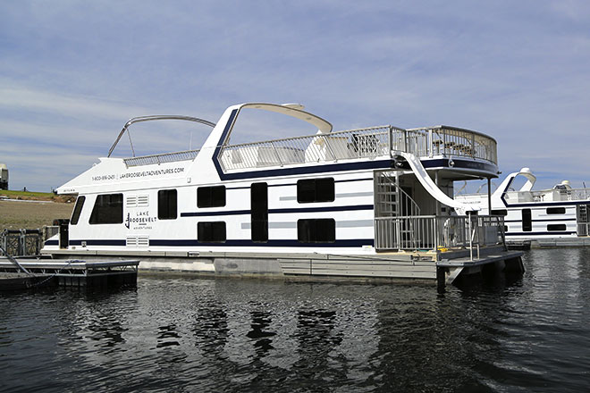 A large houseboat docked at a marina with upper deck railings.