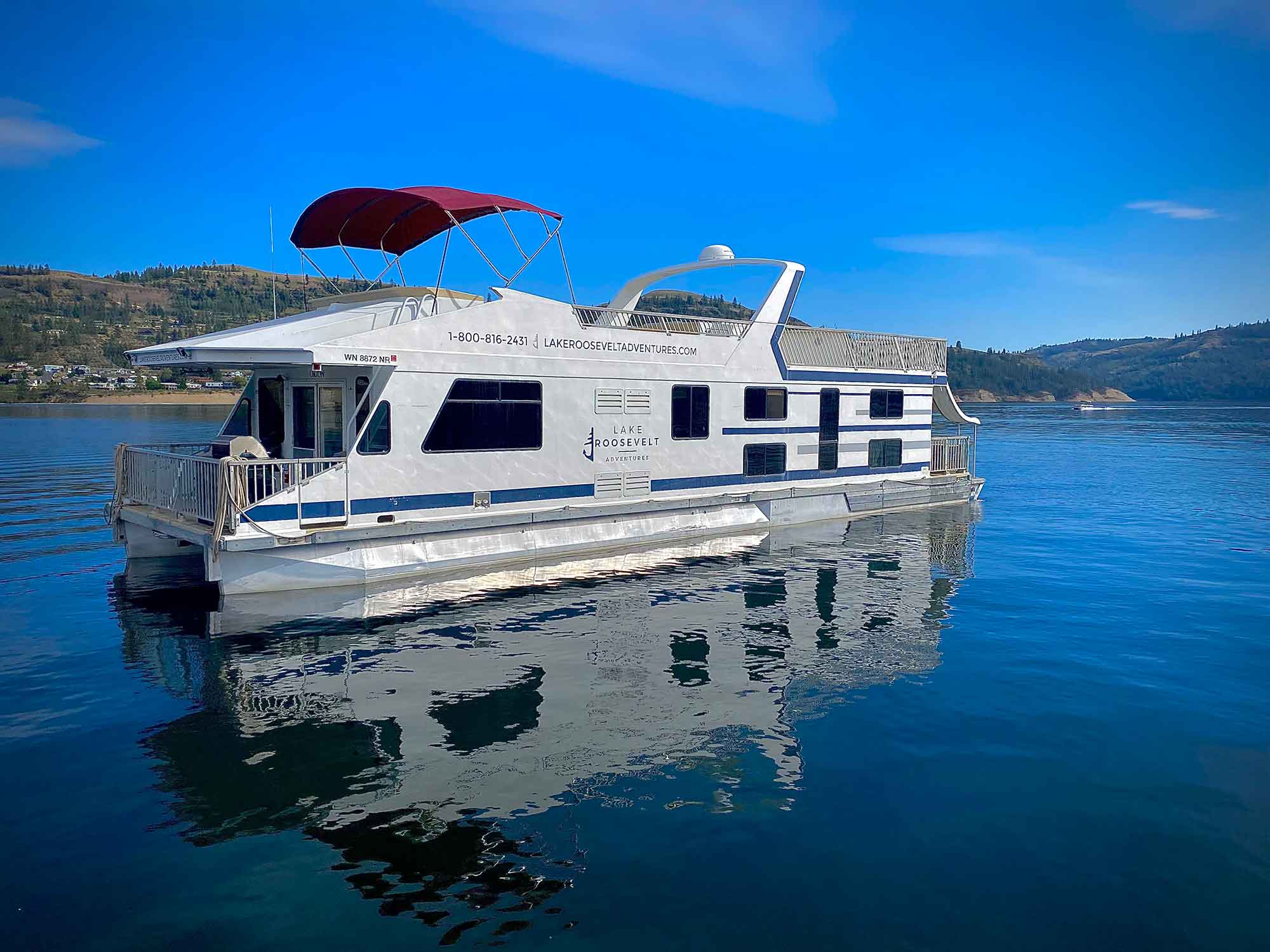 White houseboat floating on calm blue water under a clear sky.