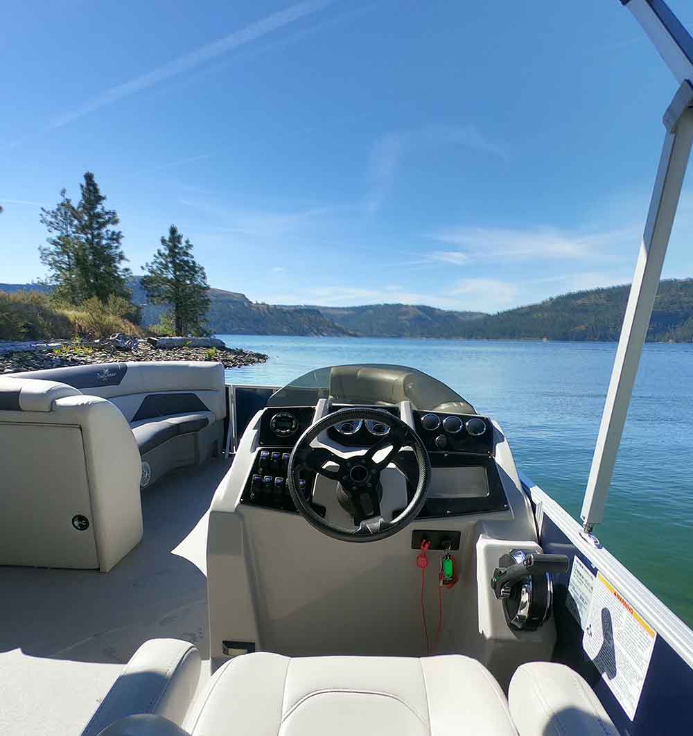 Pontoon boat steering console looking out over a bright blue lake and shoreline.