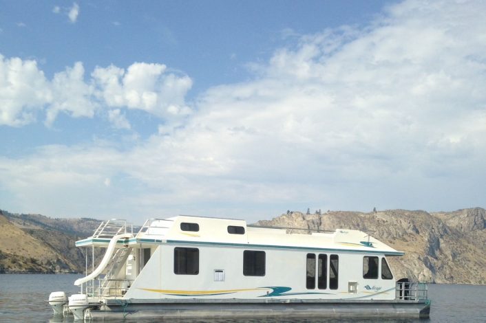 Houseboat on Lake Roosevelt with rocky hills and blue sky.