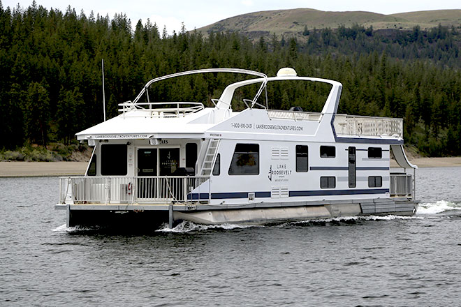 Houseboat cruising on the lake with a forested shoreline in the background.