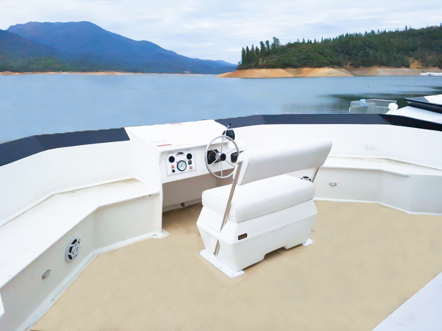Boat helm seat and steering wheel with calm lake and mountain view.