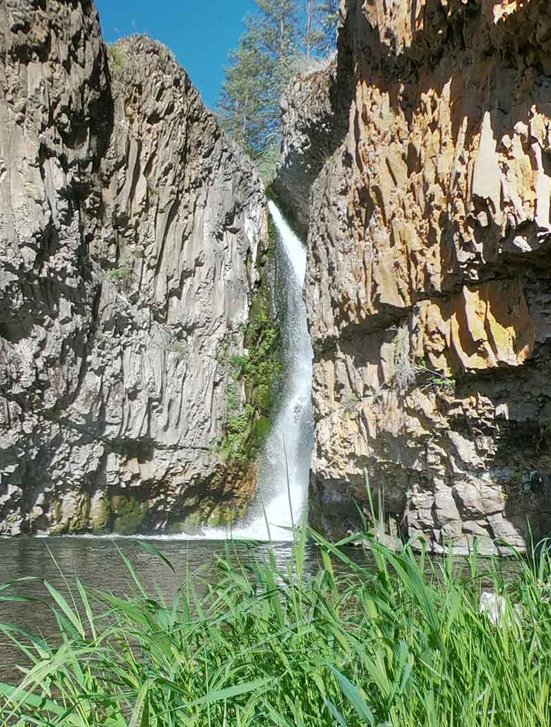 Tall waterfall pouring between steep rocky cliffs into a pool.