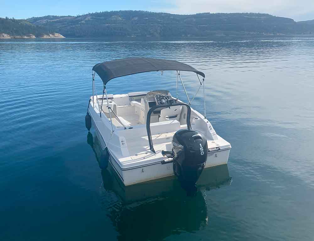 A small motorboat with canopy floating on a calm lake with mountains behind.