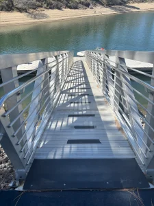 Metal access ramp with handrails leading down to a floating dock on calm water.