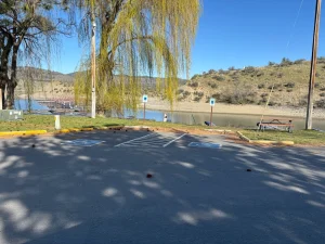 Accessible parking spaces near a lakeside path with trees, benches, and hills in view.